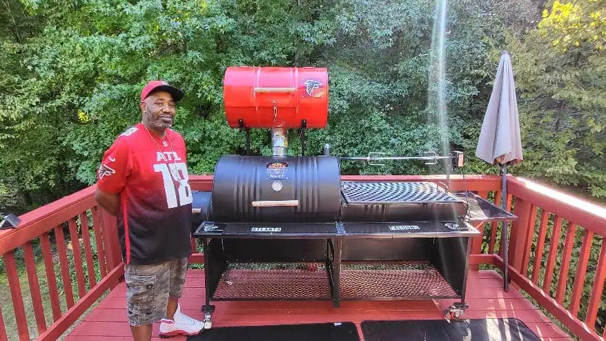 Man standing next to a large outdoor Moss Grill barbecue on a deck.