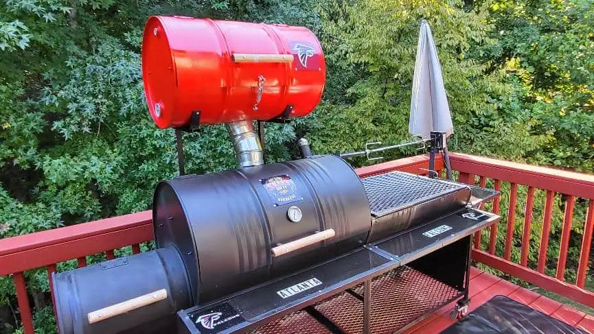 Large outdoor barbecue smoker with red and black components on a deck.