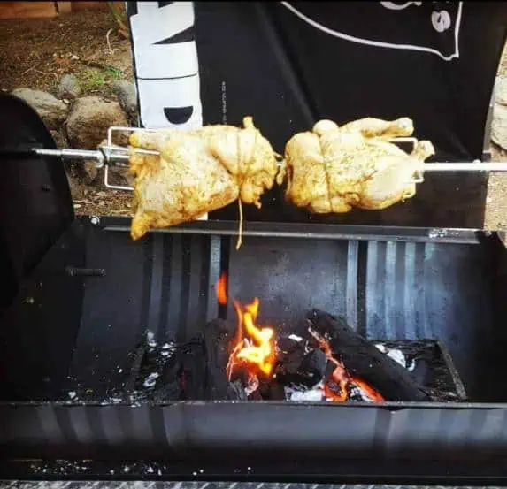 Chicken roasting on a rotisserie over a smoky fire in a Moss Grills smoker.