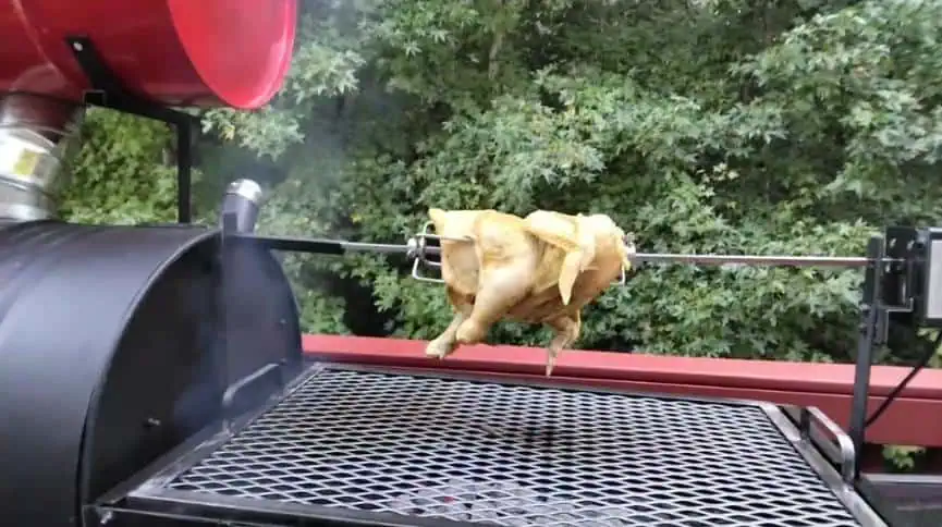 Pig roasting on Moss Grills American Queen Smoker with outdoor greenery.